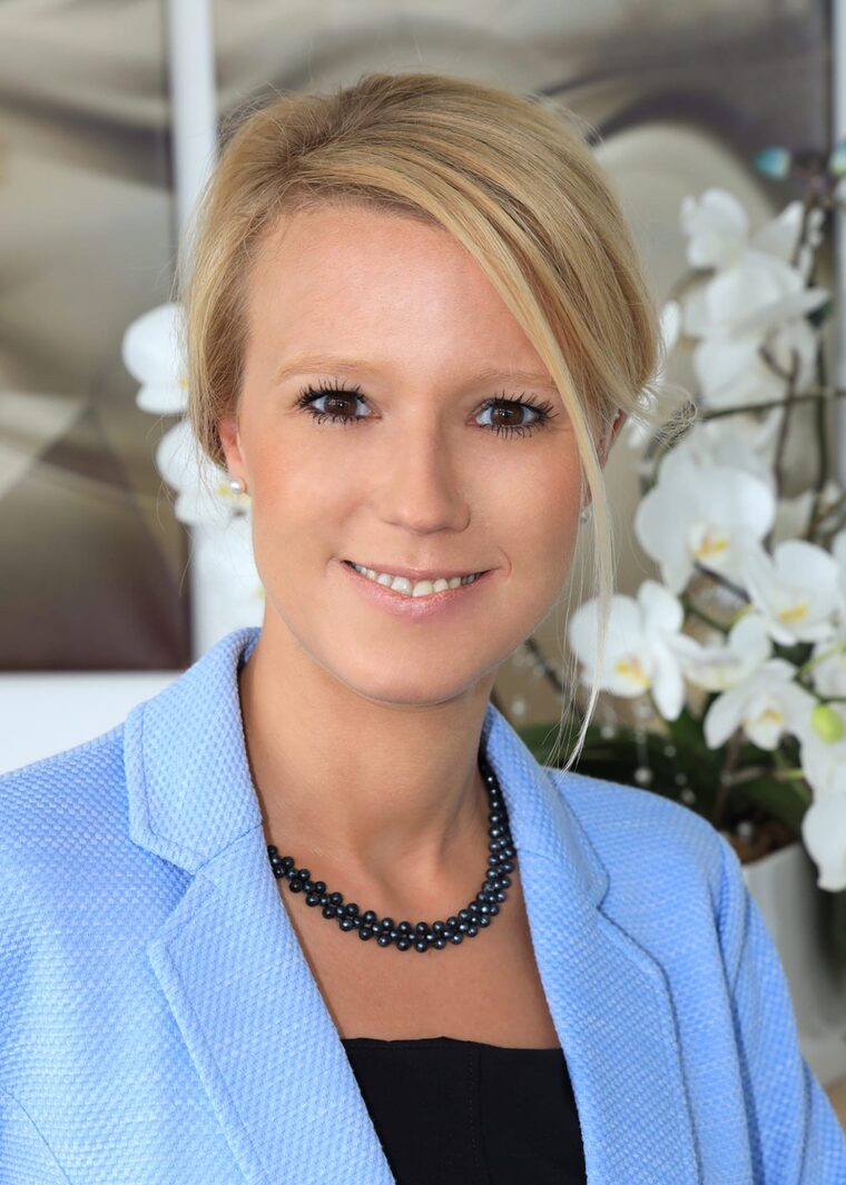 Katrin Hehl, Steuerberaterin, Porträt in hellblauem Blazer mit Perlenkette, im Hintergrund weiße Orchideen